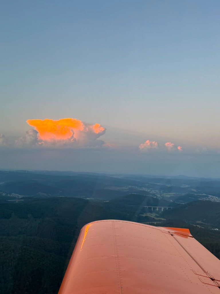 Sicht auf die Landschaft und bunte Quellwolken über der Tragfläche im Abendlicht